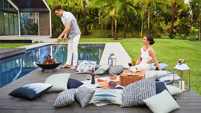 A man and a woman relaxing next to a pool with a bunch of colorful pillows by Elaine Smith.